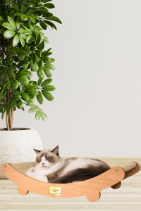 Ragdoll cat lounging on a curved sisal cat scratcher bed made of natural wood, next to a potted plant on a light wood floor.