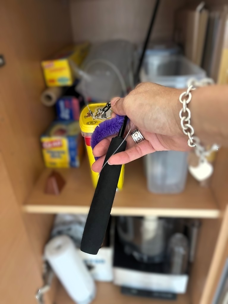 Hand putting away a purple wand toy in a cabinet.