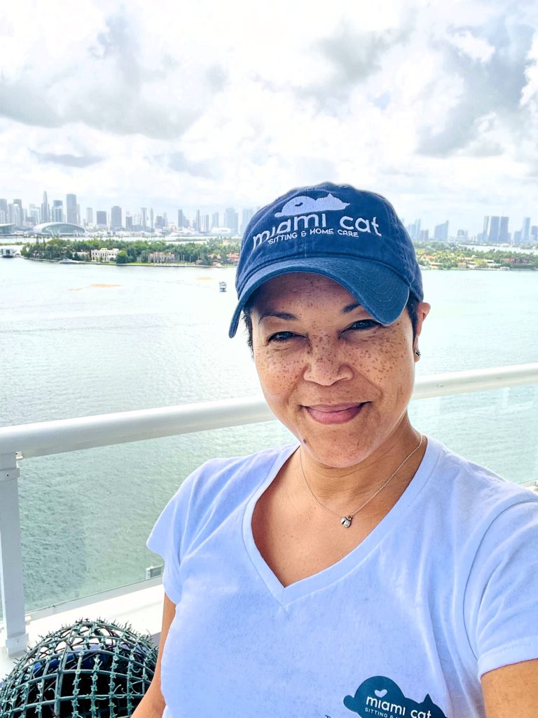 Kim, founder of Miami Cat Sitting & Home Care, wearing a branded cap with the Miami skyline in the background